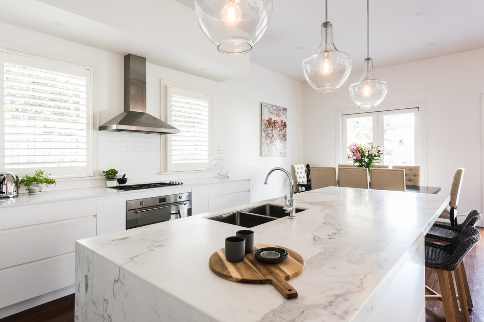 This is an example of a mid-sized contemporary single-wall open plan kitchen in Melbourne with an undermount sink, flat-panel cabinets, white cabinets, marble benchtops, white splashback, subway tile splashback, stainless steel appliances, dark hardwood floors, with island and brown floor.