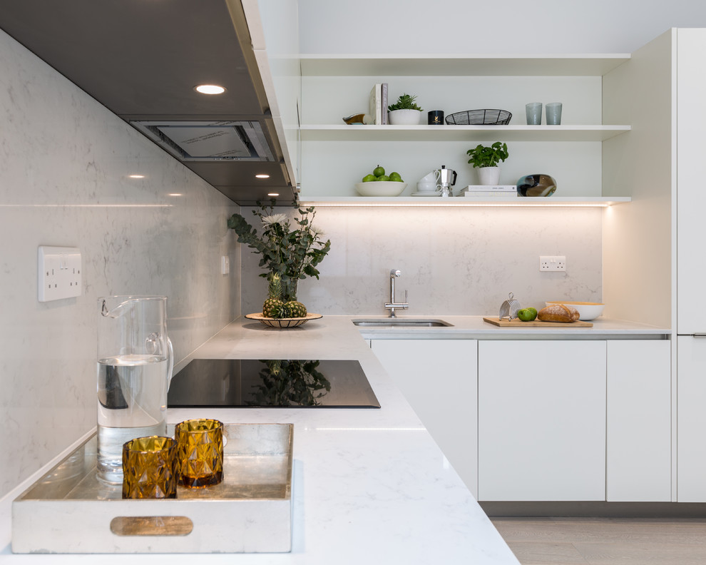 Mid-sized contemporary l-shaped eat-in kitchen in Gloucestershire with an integrated sink, flat-panel cabinets, white cabinets, solid surface benchtops, white splashback, stone slab splashback, black appliances, laminate floors, no island, brown floor and white benchtop.