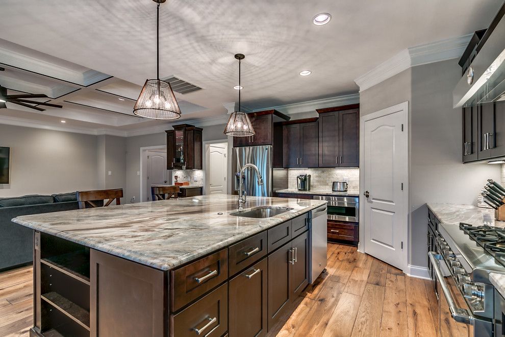 Example of a large transitional l-shaped medium tone wood floor and brown floor open concept kitchen design with an undermount sink, shaker cabinets, dark wood cabinets, granite countertops, gray backsplash, stone tile backsplash, stainless steel appliances, an island and gray countertops