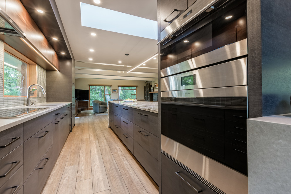 Inspiration for a mid-sized eclectic galley vinyl floor and beige floor open concept kitchen remodel in Detroit with an undermount sink, flat-panel cabinets, dark wood cabinets, granite countertops, gray backsplash, glass tile backsplash, paneled appliances, an island and gray countertops