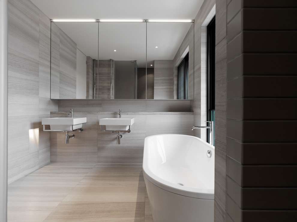 Inspiration for a modern bathroom in Melbourne with a wall-mount sink, flat-panel cabinets, a freestanding tub, stone slab, grey walls and travertine floors.