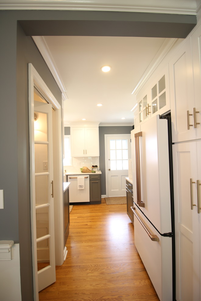 Inspiration for a mid-sized transitional u-shaped medium tone wood floor and brown floor enclosed kitchen remodel with a farmhouse sink, shaker cabinets, white cabinets, quartz countertops, white backsplash, subway tile backsplash, white appliances, no island and beige countertops