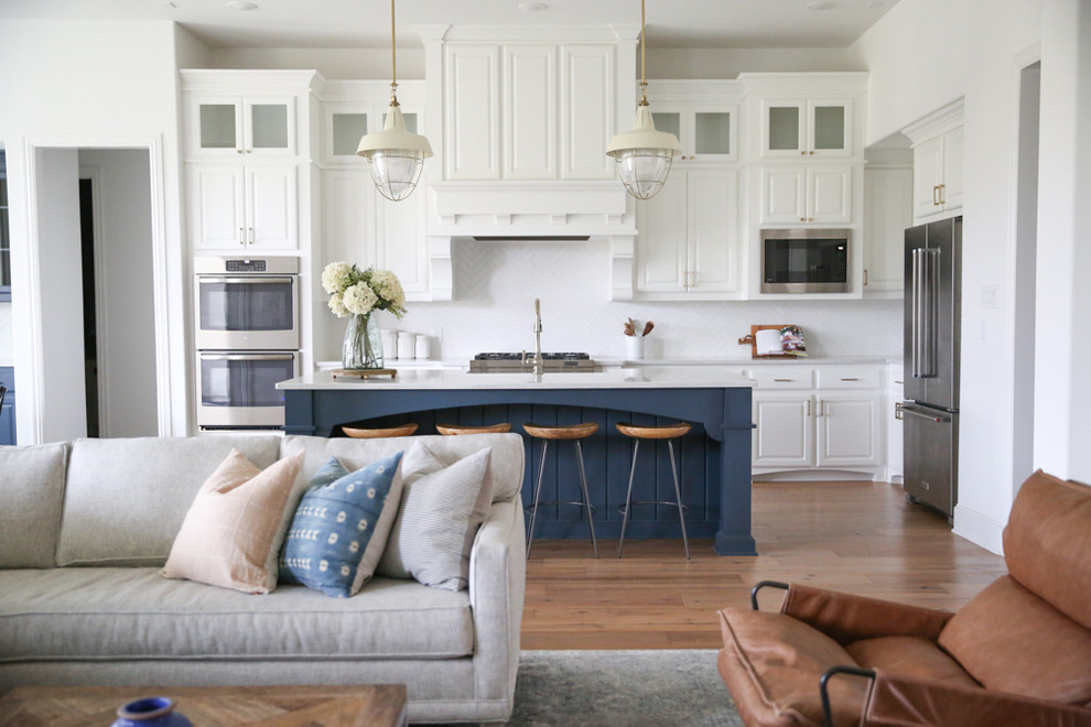 Inspiration for a large transitional u-shaped medium tone wood floor and brown floor eat-in kitchen remodel in Dallas with a farmhouse sink, raised-panel cabinets, white cabinets, quartz countertops, white backsplash, ceramic backsplash, stainless steel appliances, an island and white countertops