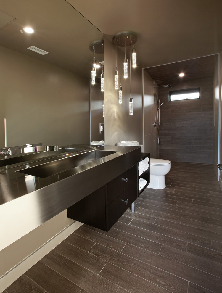 Design ideas for a large modern 3/4 bathroom in Orange County with open cabinets, dark wood cabinets, a curbless shower, a two-piece toilet, gray tile, porcelain tile, beige walls, porcelain floors, an integrated sink, stainless steel benchtops, brown floor and an open shower.