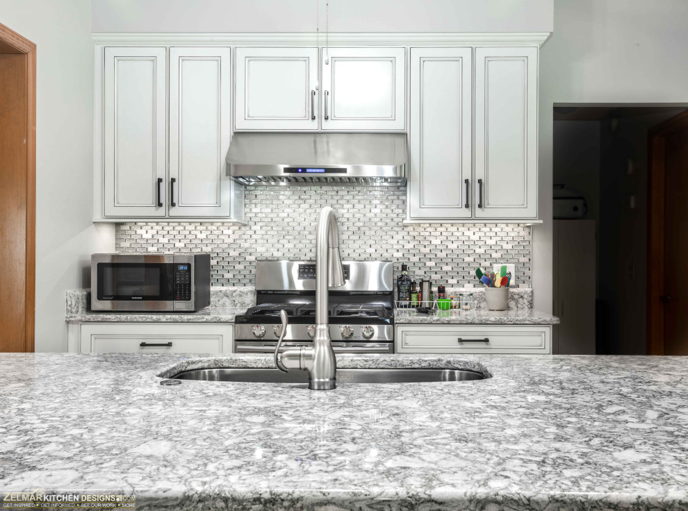 Inspiration for a mid-sized transitional single-wall eat-in kitchen in Orlando with an undermount sink, recessed-panel cabinets, white cabinets, quartz benchtops, grey splashback, glass tile splashback, with island and grey benchtop.