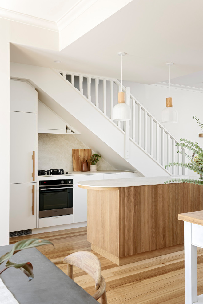 Photo of a small scandi galley kitchen/diner in Perth with a submerged sink, flat-panel cabinets, white cabinets, engineered stone countertops, beige splashback, porcelain splashback, black appliances, light hardwood flooring, an island, brown floors, beige worktops and a vaulted ceiling.