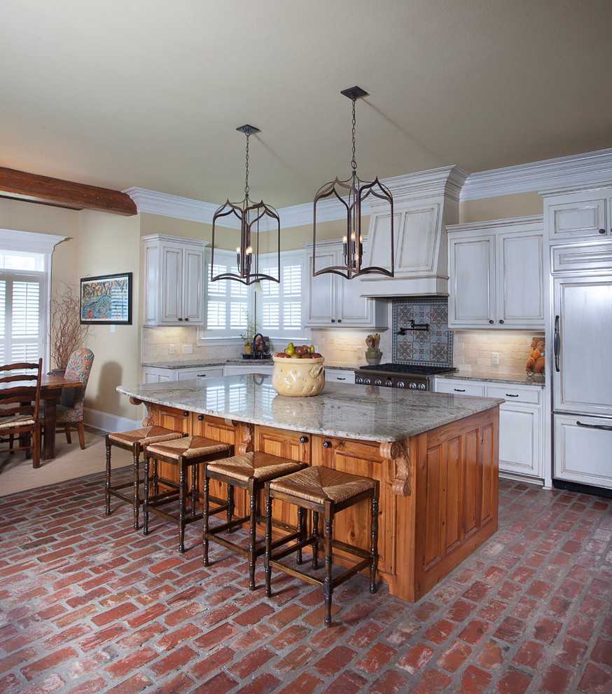 This is an example of a traditional eat-in kitchen in New Orleans with raised-panel cabinets, white cabinets, beige splashback, panelled appliances, brick floors, with island and travertine splashback.
