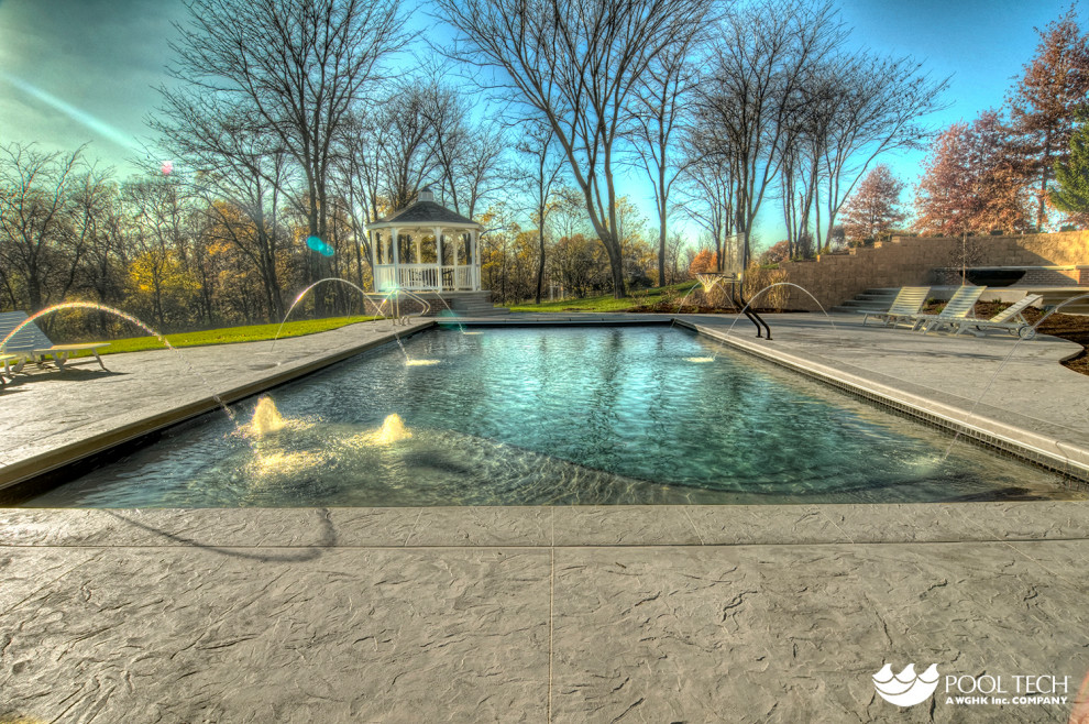 На фото: большой прямоугольный бассейн на заднем дворе в стиле рустика с фонтаном и покрытием из декоративного бетона