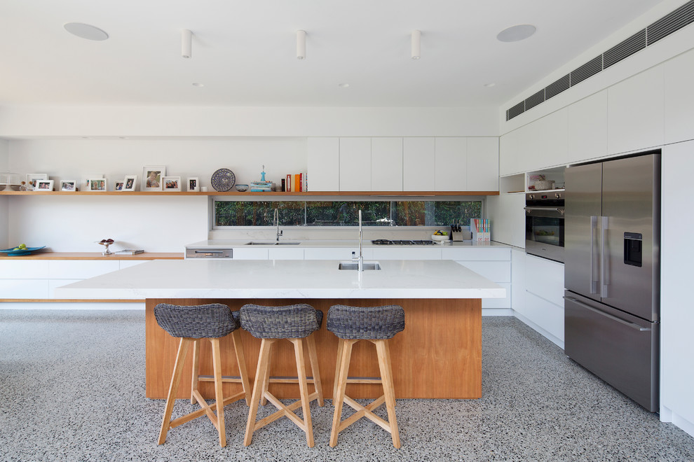 This is an example of a large contemporary l-shaped open plan kitchen in Sydney with a double-bowl sink, flat-panel cabinets, white cabinets, solid surface benchtops, stainless steel appliances, concrete floors and with island.