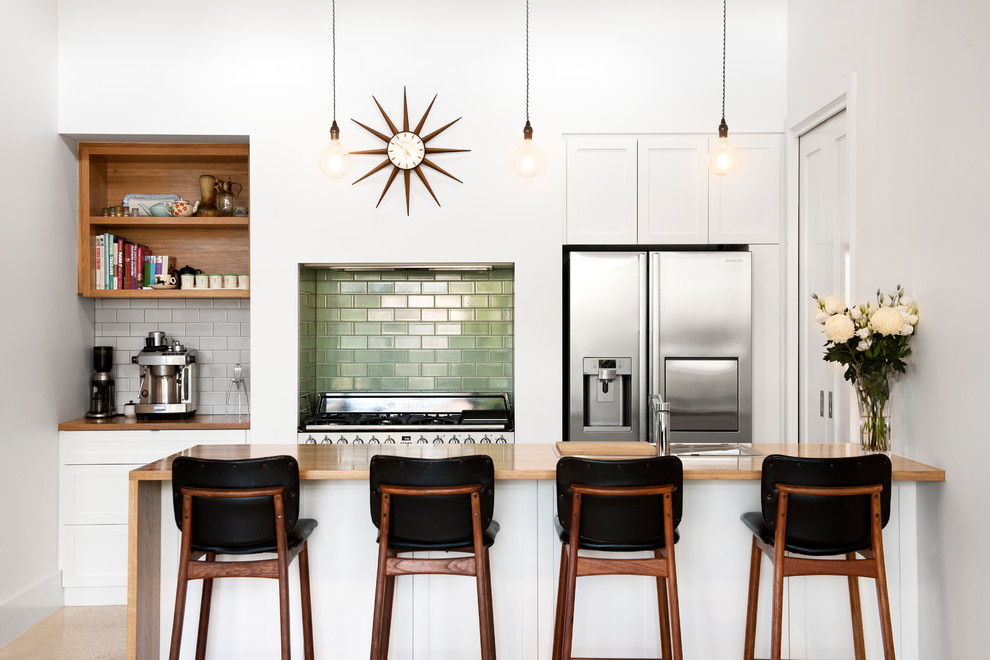 Photo of a contemporary galley kitchen in Adelaide with a drop-in sink, flat-panel cabinets, white cabinets, wood benchtops, green splashback, subway tile splashback, stainless steel appliances, a peninsula, beige floor and brown benchtop.