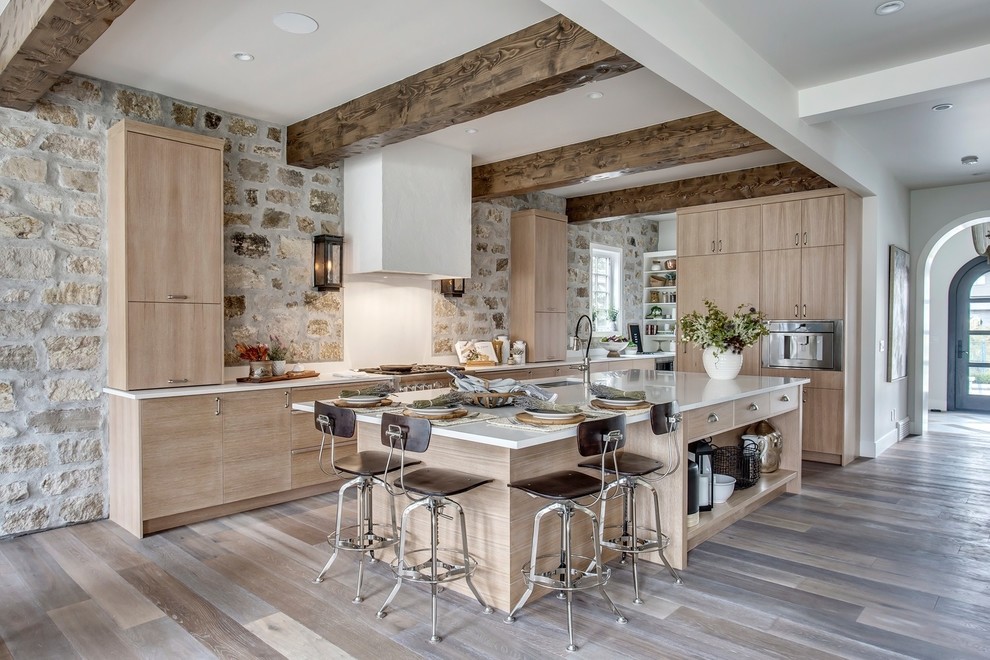 Inspiration for a large country l-shaped kitchen in Calgary with flat-panel cabinets, quartz benchtops, white splashback, medium hardwood floors, with island, white benchtop, an undermount sink, light wood cabinets, stainless steel appliances and brown floor.