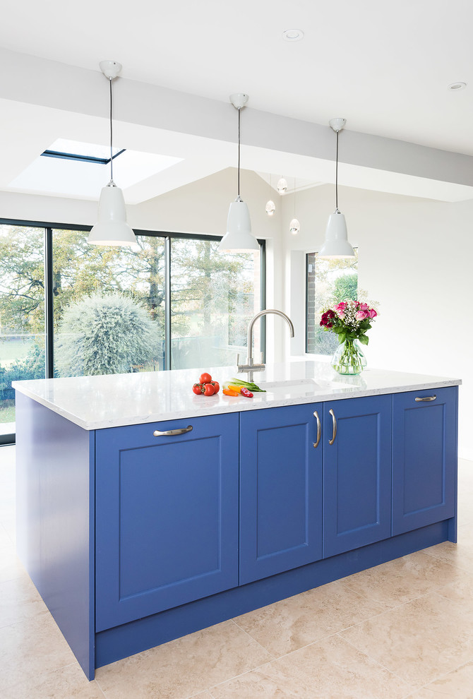 Photo of a large transitional single-wall open plan kitchen in Buckinghamshire with a double-bowl sink, shaker cabinets, blue cabinets, quartzite benchtops, white splashback, subway tile splashback, black appliances, porcelain floors, with island, beige floor and yellow benchtop.