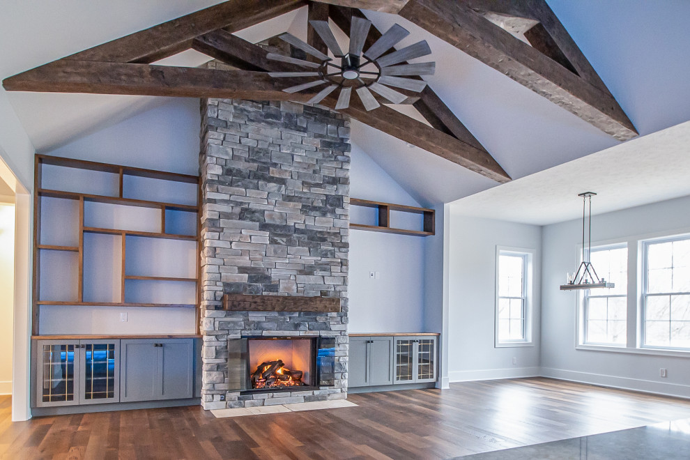 Expansive classic open plan living room in Cleveland with grey walls, medium hardwood flooring, a standard fireplace, a stone fireplace surround, brown floors and exposed beams.