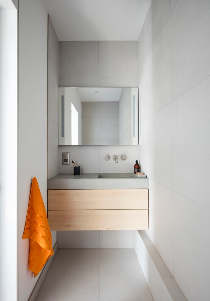 Photo of a small modern wet room bathroom in London with light wood cabinets, a wall-mount toilet, porcelain tile, grey walls, porcelain floors, concrete benchtops, grey floor, an open shower, flat-panel cabinets, a drop-in tub, gray tile, a wall-mount sink, grey benchtops, a single vanity and a floating vanity.