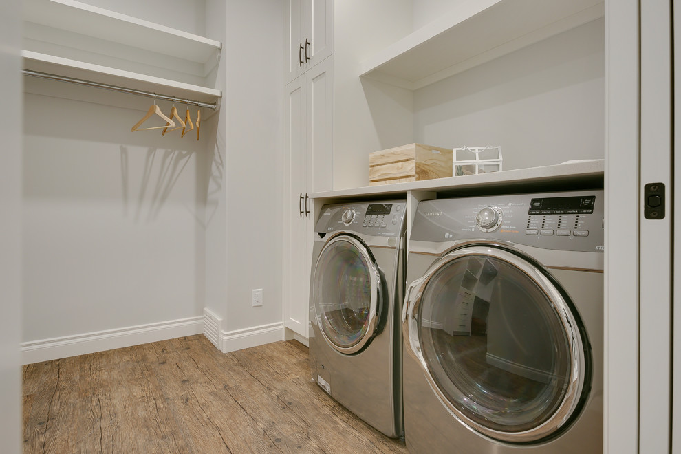 This is an example of a large transitional l-shaped laundry cupboard in Calgary with shaker cabinets, white cabinets, quartzite benchtops, grey walls, vinyl floors, a side-by-side washer and dryer, brown floor and white benchtop.