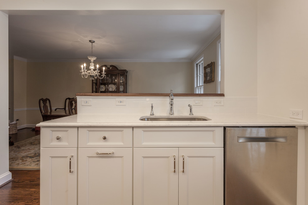 Photo of a mid-sized transitional u-shaped eat-in kitchen in DC Metro with a single-bowl sink, shaker cabinets, white cabinets, quartz benchtops, white splashback, subway tile splashback, stainless steel appliances, light hardwood floors, a peninsula, brown floor and white benchtop.