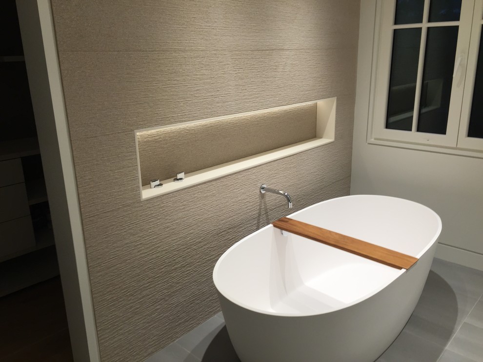 Photo of a large contemporary master bathroom in Boston with white cabinets, a freestanding tub, a curbless shower, a wall-mount toilet, beige tile, ceramic tile, beige walls and concrete floors.