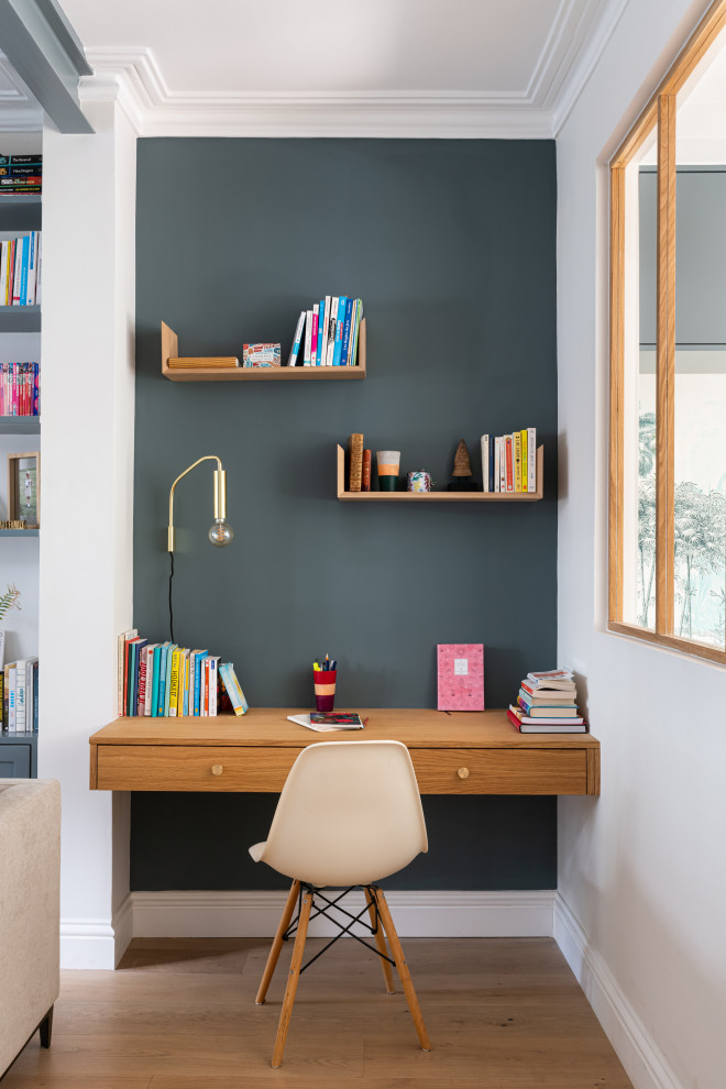 Exempel på ett litet eklektiskt hemmabibliotek, med blå väggar, ljust trägolv, ett inbyggt skrivbord och beiget golv