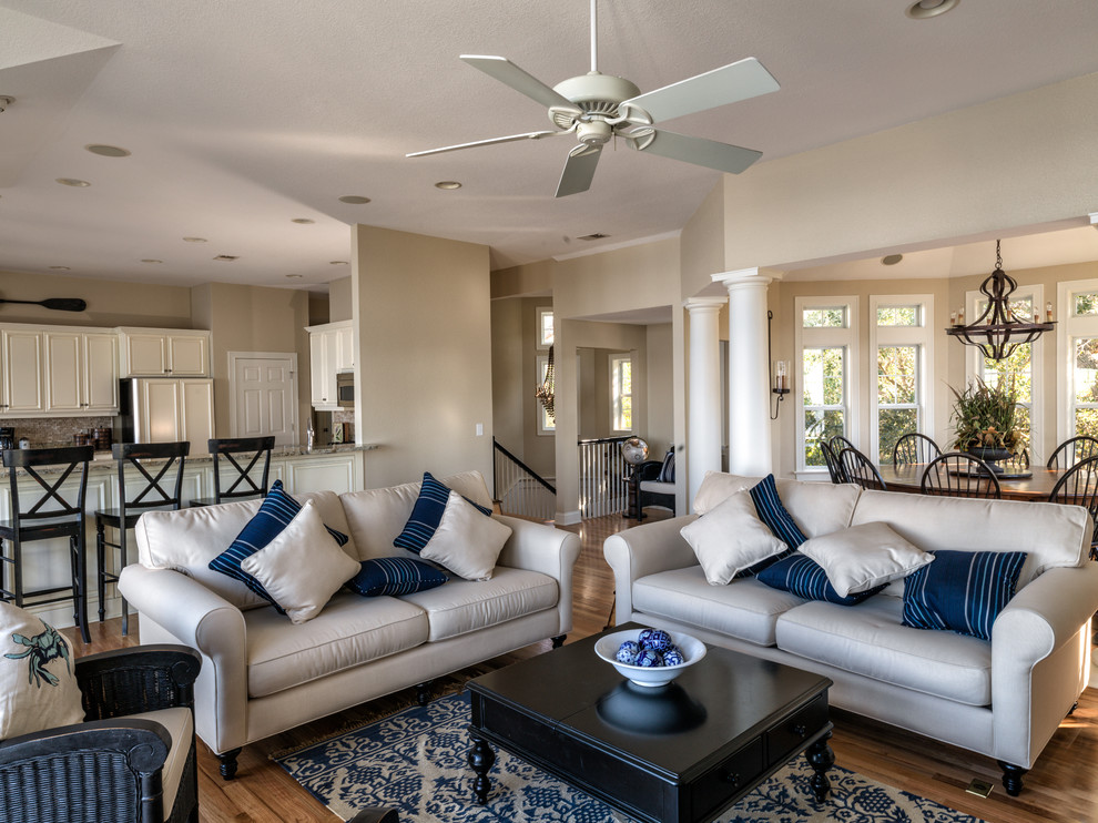 Photo of a large beach style open concept family room in Other with beige walls, medium hardwood floors, a standard fireplace, a stone fireplace surround and a wall-mounted tv.
