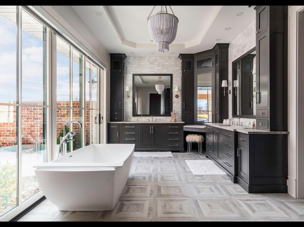 Inspiration for a large country master bathroom in Other with recessed-panel cabinets, black cabinets, a freestanding tub, gray tile, subway tile, ceramic floors, an undermount sink, marble benchtops, grey floor and grey benchtops.