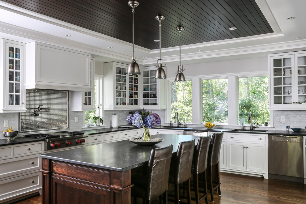 Traditional l-shaped kitchen in Boston with glass-front cabinets, white cabinets, metallic splashback, metal splashback, stainless steel appliances, dark hardwood floors, with island, brown floor and black benchtop.