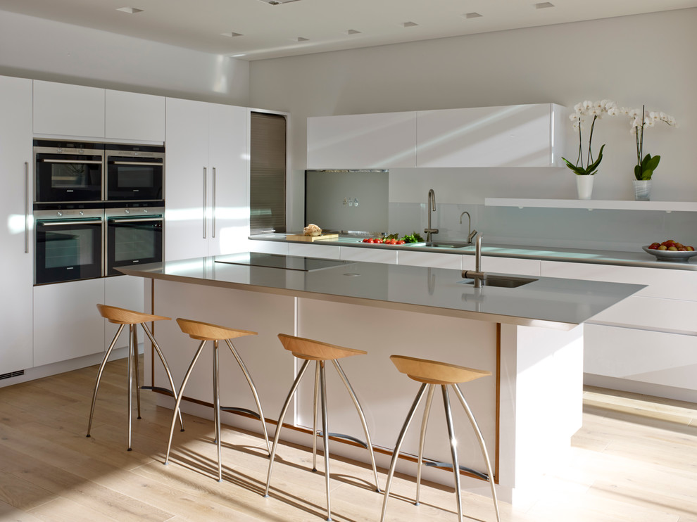 Design ideas for a large contemporary open plan kitchen in London with an undermount sink, flat-panel cabinets, solid surface benchtops, glass sheet splashback, stainless steel appliances and with island.
