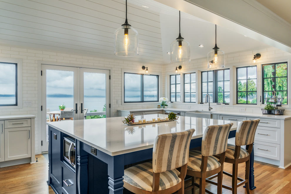 Inspiration for a large beach style u-shaped open plan kitchen in Seattle with a farmhouse sink, shaker cabinets, white cabinets, quartz benchtops, white splashback, subway tile splashback, stainless steel appliances, medium hardwood floors, with island, white benchtop and vaulted.