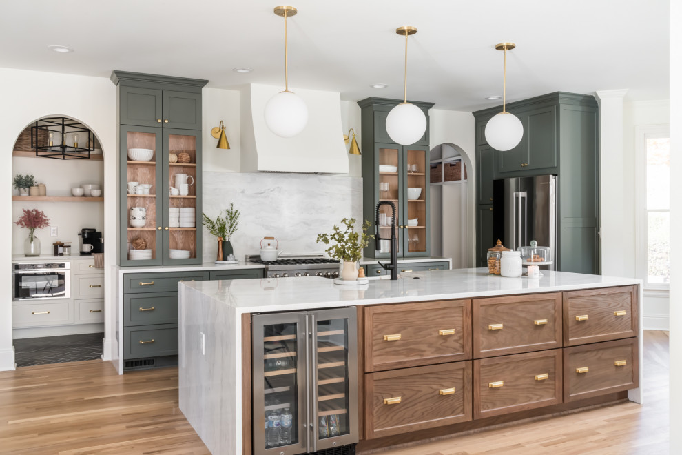 Photo of a large transitional single-wall open plan kitchen in Atlanta with a farmhouse sink, shaker cabinets, green cabinets, quartzite benchtops, white splashback, engineered quartz splashback, stainless steel appliances, light hardwood floors, with island and white benchtop.