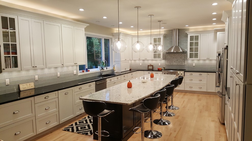 Mid-sized transitional single-wall light wood floor and yellow floor eat-in kitchen photo with an undermount sink, shaker cabinets, white cabinets, quartz countertops, gray backsplash, glass tile backsplash, stainless steel appliances and an island