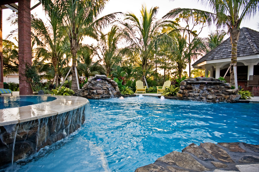 Mid-sized tropical backyard custom-shaped pool in Miami with a hot tub and natural stone pavers.