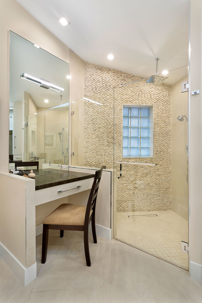 This is an example of a mid-sized contemporary master bathroom in Miami with flat-panel cabinets, beige cabinets, a corner shower, a one-piece toilet, beige tile, pebble tile, beige walls, ceramic floors, an undermount sink, terrazzo benchtops, beige floor, a hinged shower door and black benchtops.