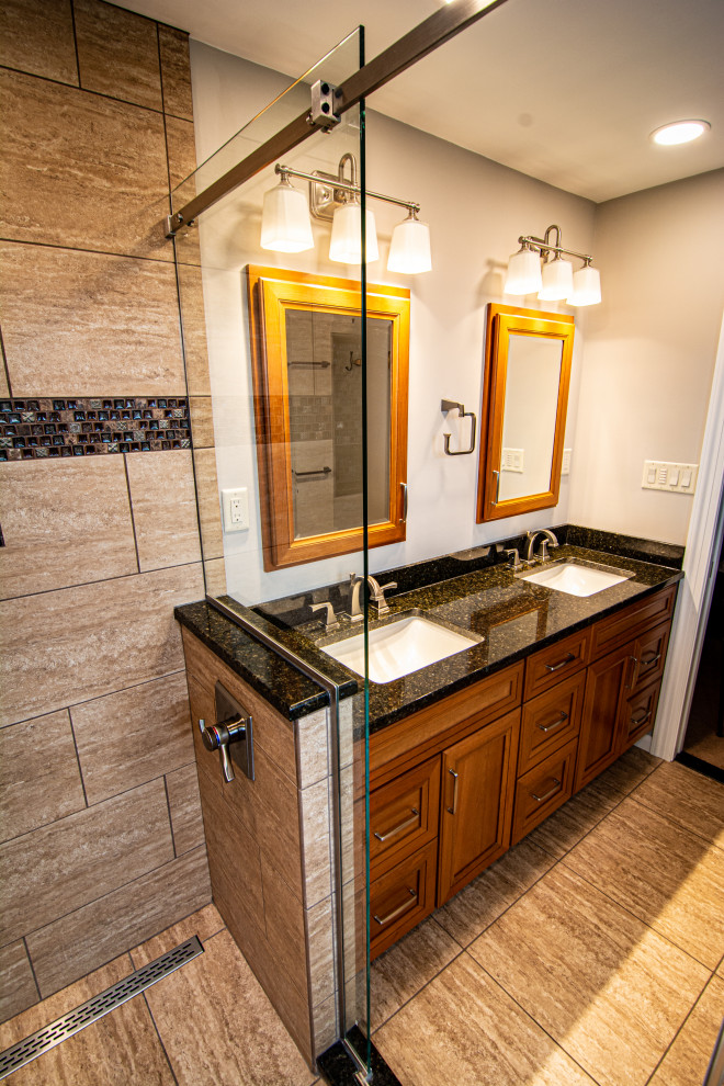 Mid-sized traditional master bathroom in Philadelphia with flat-panel cabinets, medium wood cabinets, an alcove shower, a two-piece toilet, brown tile, porcelain tile, porcelain floors, an undermount sink, granite benchtops, brown floor, a sliding shower screen, black benchtops, a shower seat, a double vanity and a built-in vanity.