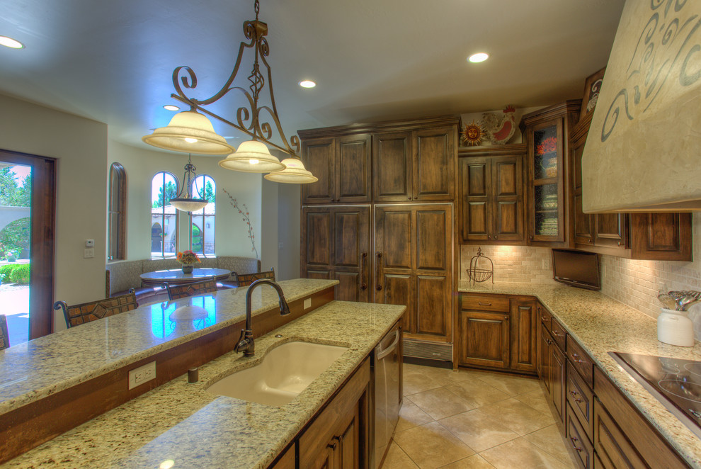 Country u-shaped kitchen in Albuquerque with raised-panel cabinets, brown cabinets, granite benchtops, beige splashback, stone tile splashback, stainless steel appliances, with island, an undermount sink and ceramic floors.