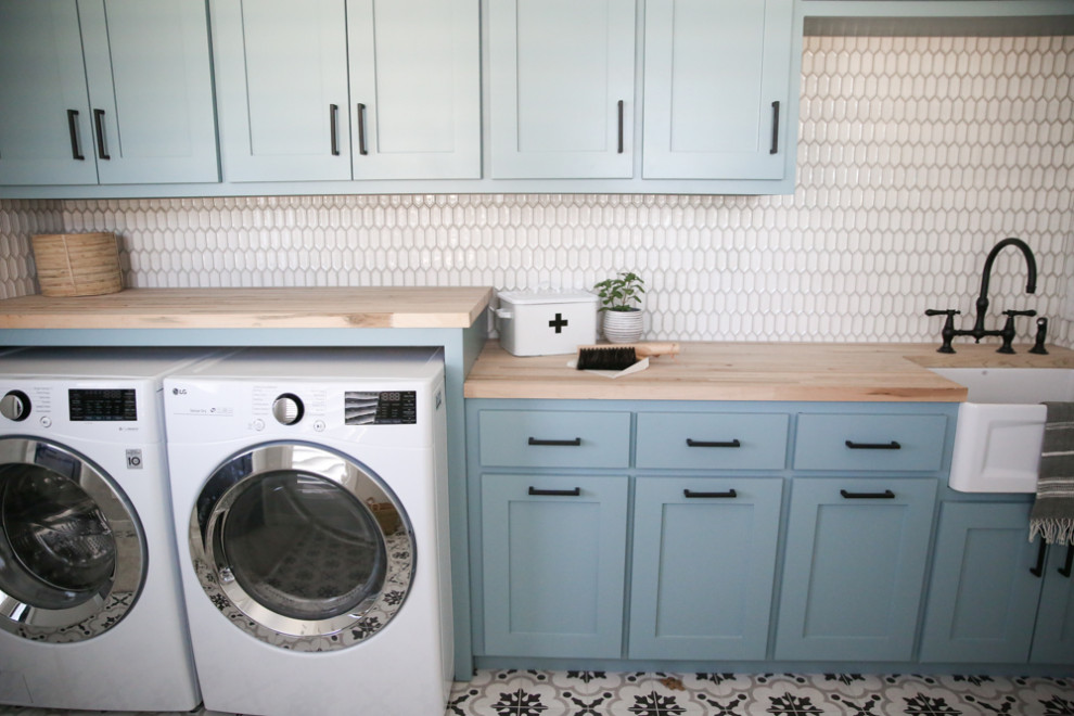 Inspiration for a mid-sized traditional single-wall dedicated laundry room in Dallas with recessed-panel cabinets, blue cabinets, wood benchtops, grey walls, ceramic floors, a side-by-side washer and dryer, multi-coloured floor and brown benchtop.