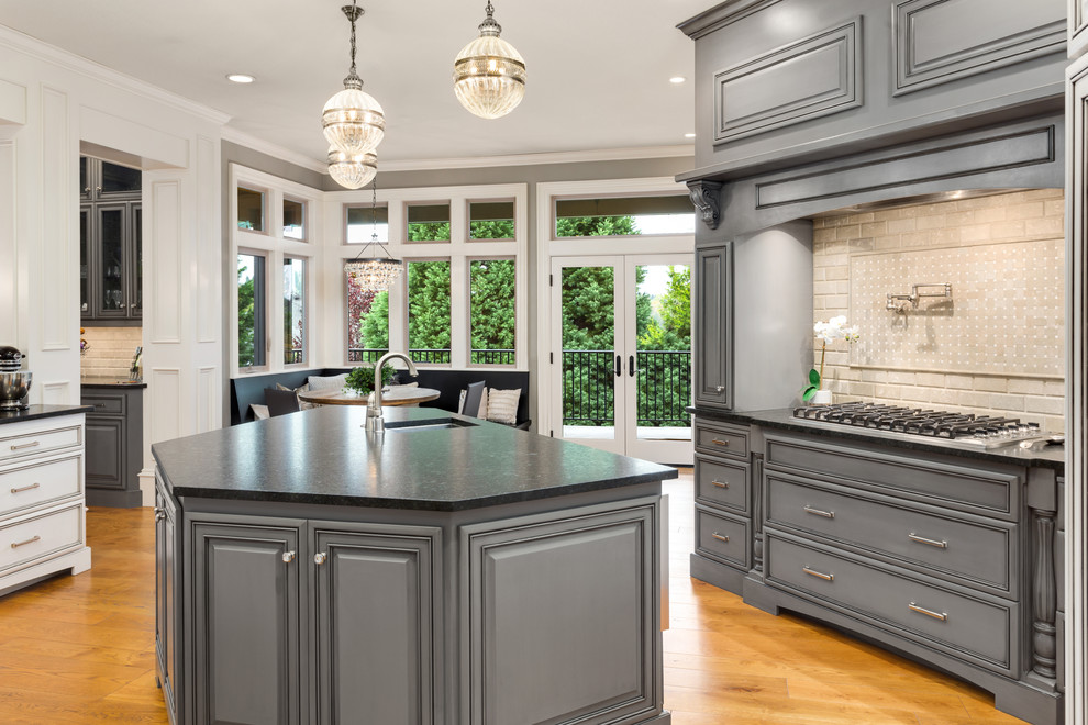 This is an example of a transitional eat-in kitchen in Portland with an undermount sink, beaded inset cabinets, grey cabinets, beige splashback, subway tile splashback, medium hardwood floors, with island and black benchtop.