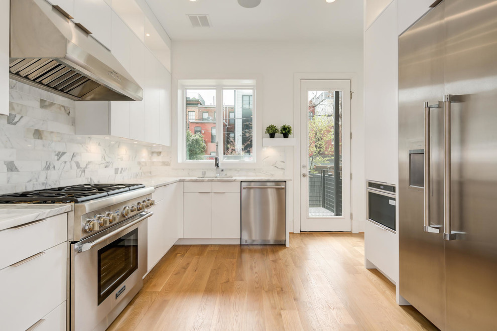 This is an example of a mid-sized transitional u-shaped kitchen in DC Metro with an undermount sink, flat-panel cabinets, white cabinets, white splashback, stainless steel appliances, medium hardwood floors, no island, brown floor, white benchtop, marble benchtops and marble splashback.