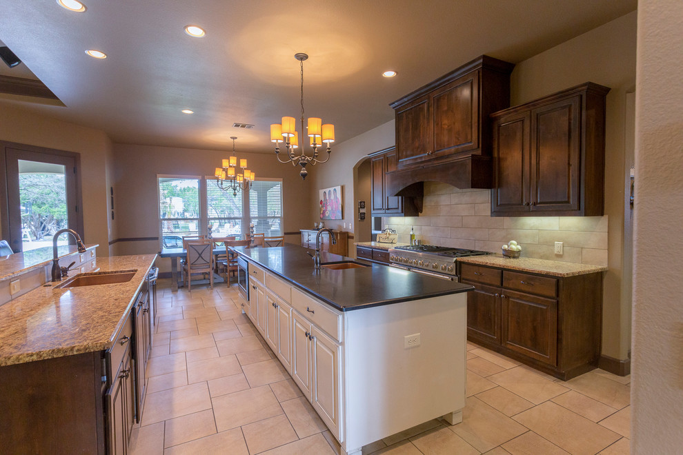 Example of a large transitional galley porcelain tile and beige floor eat-in kitchen design in Austin with an undermount sink, raised-panel cabinets, dark wood cabinets, granite countertops, beige backsplash, porcelain backsplash, stainless steel appliances and two islands