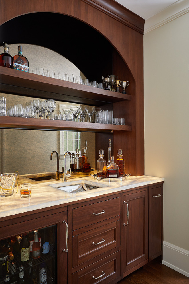 This is an example of a traditional single-wall wet bar in Grand Rapids with an undermount sink, medium wood cabinets, onyx benchtops, mirror splashback and medium hardwood floors.