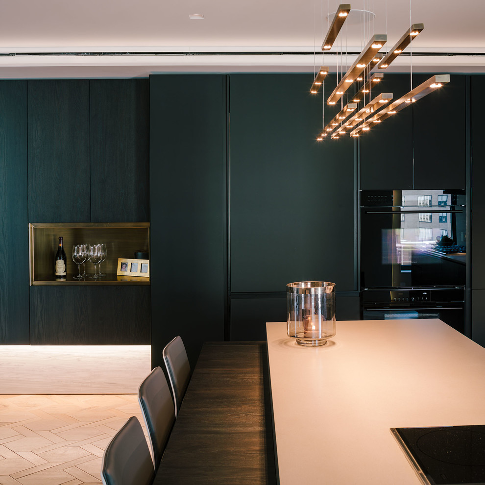 This is an example of a large modern single-wall open plan kitchen in New York with an undermount sink, flat-panel cabinets, black cabinets, concrete benchtops, grey splashback, stone slab splashback, black appliances, light hardwood floors, with island and beige floor.
