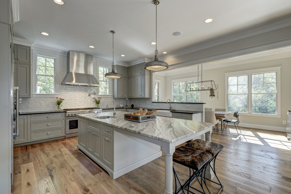 Photo of an expansive modern l-shaped kitchen in DC Metro with a farmhouse sink, raised-panel cabinets, grey cabinets, marble benchtops, white splashback, subway tile splashback, stainless steel appliances, light hardwood floors and with island.