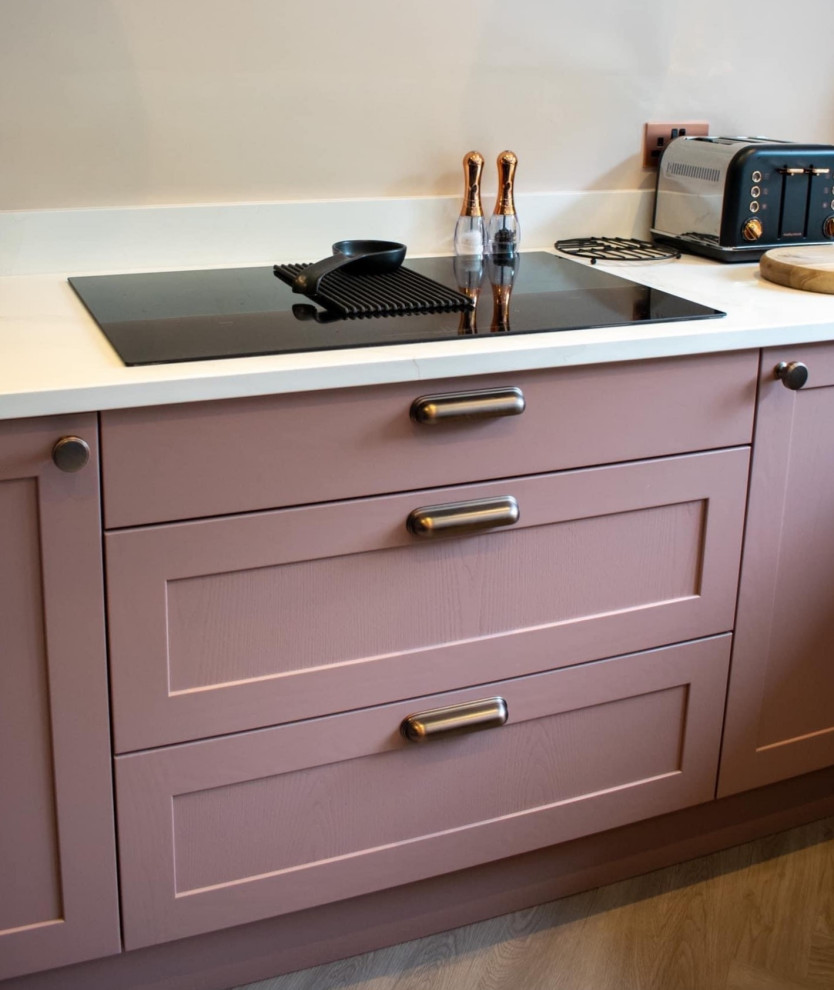This is an example of a medium sized modern u-shaped open plan kitchen in Other with an integrated sink, shaker cabinets, quartz worktops, white splashback, black appliances, a breakfast bar, brown floors, white worktops, feature lighting and pink cabinets.