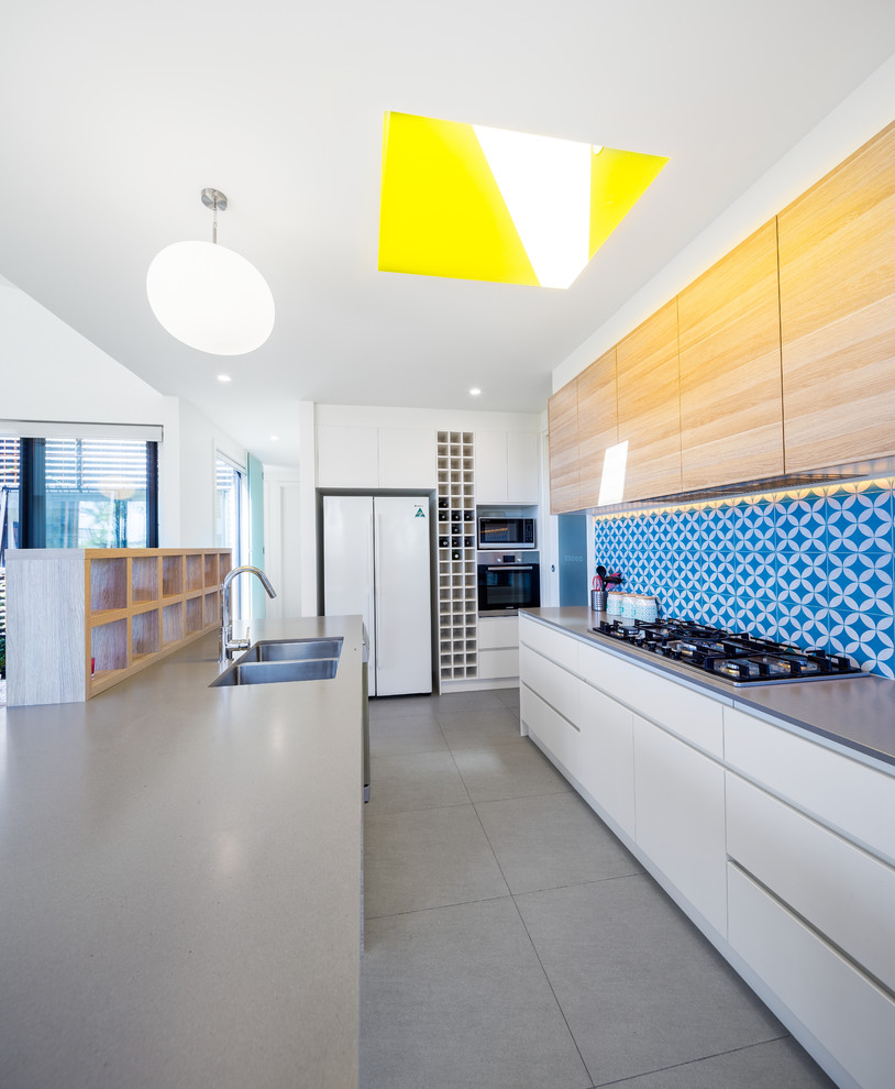 Mid-sized contemporary galley open plan kitchen in Canberra - Queanbeyan with white cabinets, quartz benchtops, blue splashback, cement tile splashback, with island, grey floor, a double-bowl sink, flat-panel cabinets, white appliances and grey benchtop.