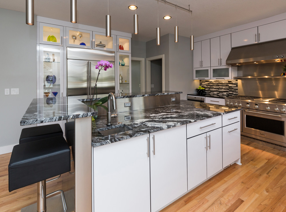 Example of a large trendy u-shaped light wood floor open concept kitchen design with an undermount sink, flat-panel cabinets, white cabinets, granite countertops, multicolored backsplash, mosaic tile backsplash, stainless steel appliances and an island