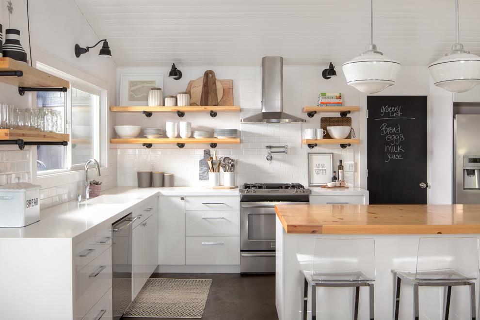 Photo of a country l-shaped kitchen in Sacramento with an integrated sink, flat-panel cabinets, white cabinets, wood benchtops, white splashback, subway tile splashback, stainless steel appliances and with island.