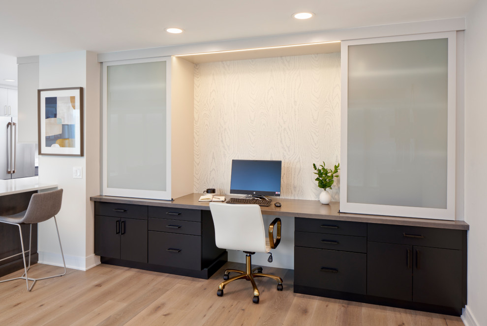 Photo of a small contemporary study room in Chicago with white walls, light hardwood floors, a built-in desk, brown floor and wallpaper.