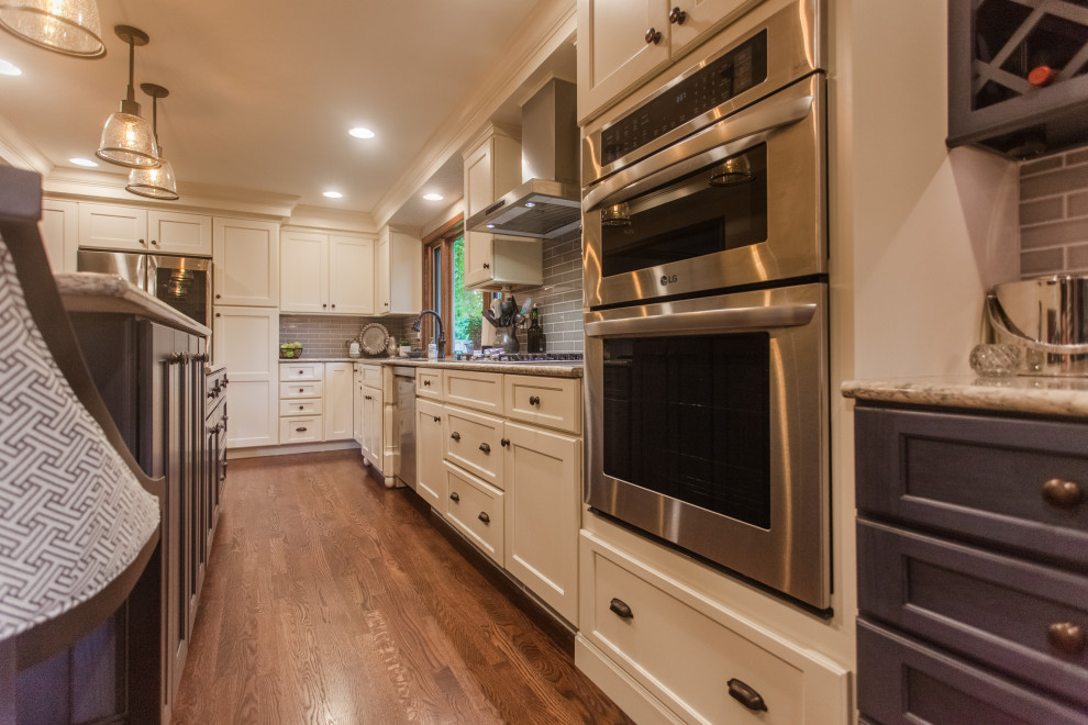 Large transitional single-wall dark wood floor, brown floor and coffered ceiling eat-in kitchen photo in Cincinnati with a double-bowl sink, shaker cabinets, white cabinets, granite countertops, gray backsplash, subway tile backsplash, stainless steel appliances, an island and multicolored countertops