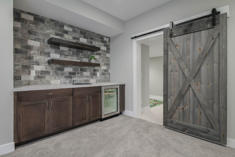 Mid-sized country single-wall wet bar in Grand Rapids with a drop-in sink, shaker cabinets, dark wood cabinets, laminate benchtops, grey splashback, brick splashback, carpet, grey floor and grey benchtop.