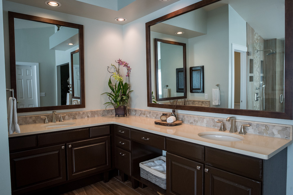 This is an example of a large transitional master bathroom in Denver with furniture-like cabinets, brown cabinets, a freestanding tub, a corner shower, a one-piece toilet, beige tile, pebble tile, green walls, porcelain floors, an undermount sink and engineered quartz benchtops.