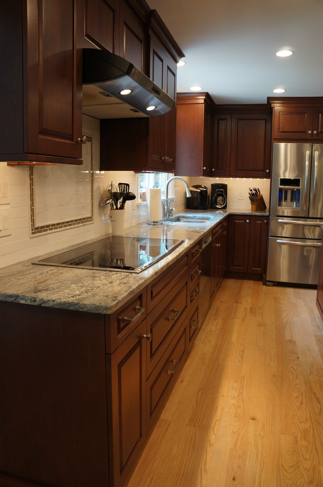Example of a mid-sized transitional galley light wood floor eat-in kitchen design in Boston with an undermount sink, raised-panel cabinets, dark wood cabinets, quartz countertops, white backsplash, ceramic backsplash, stainless steel appliances and an island