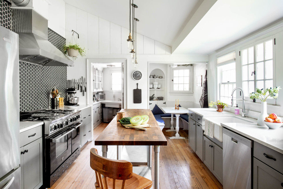 Country galley kitchen in Other with a farmhouse sink, shaker cabinets, grey cabinets, black splashback, mosaic tile splashback, stainless steel appliances, medium hardwood floors, with island, brown floor and white benchtop.